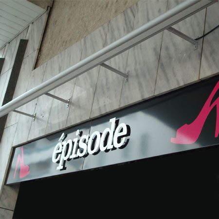 Lettrage épisode en relief sur une façade en pierre de commerce de prêt-à-porter