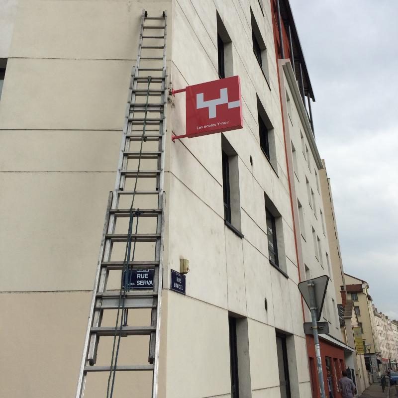 Intervention de pose d'enseigne sur une façade d'immeuble avec échelle de couvreur