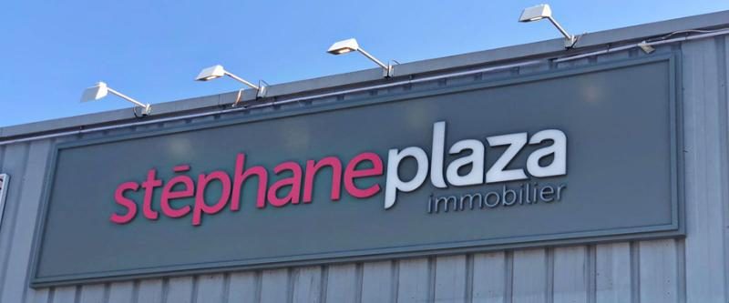 Enseigne lumineuse bleue Stephane Plaza Immobilier posée en façade d'agence