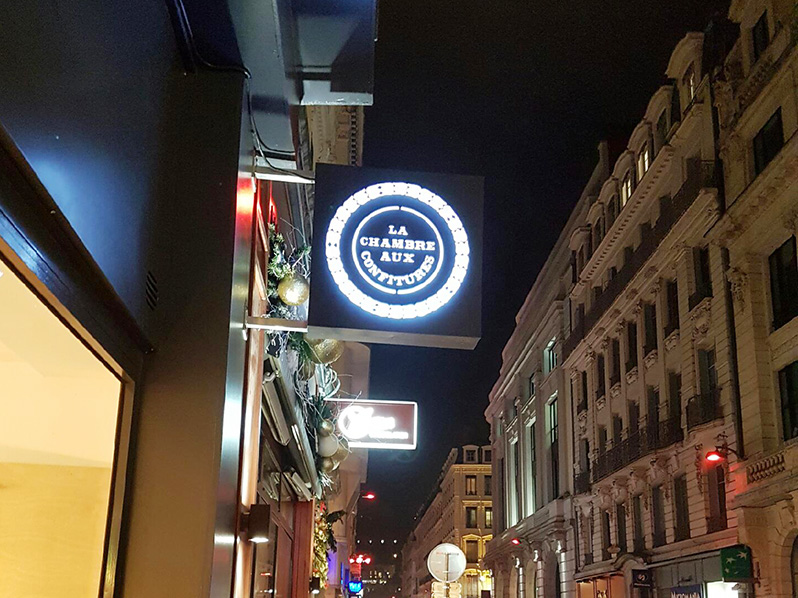 Caisson lumineux rond Le Caveau des 4Vents éclairé de nuit sur une façade lyonnaise